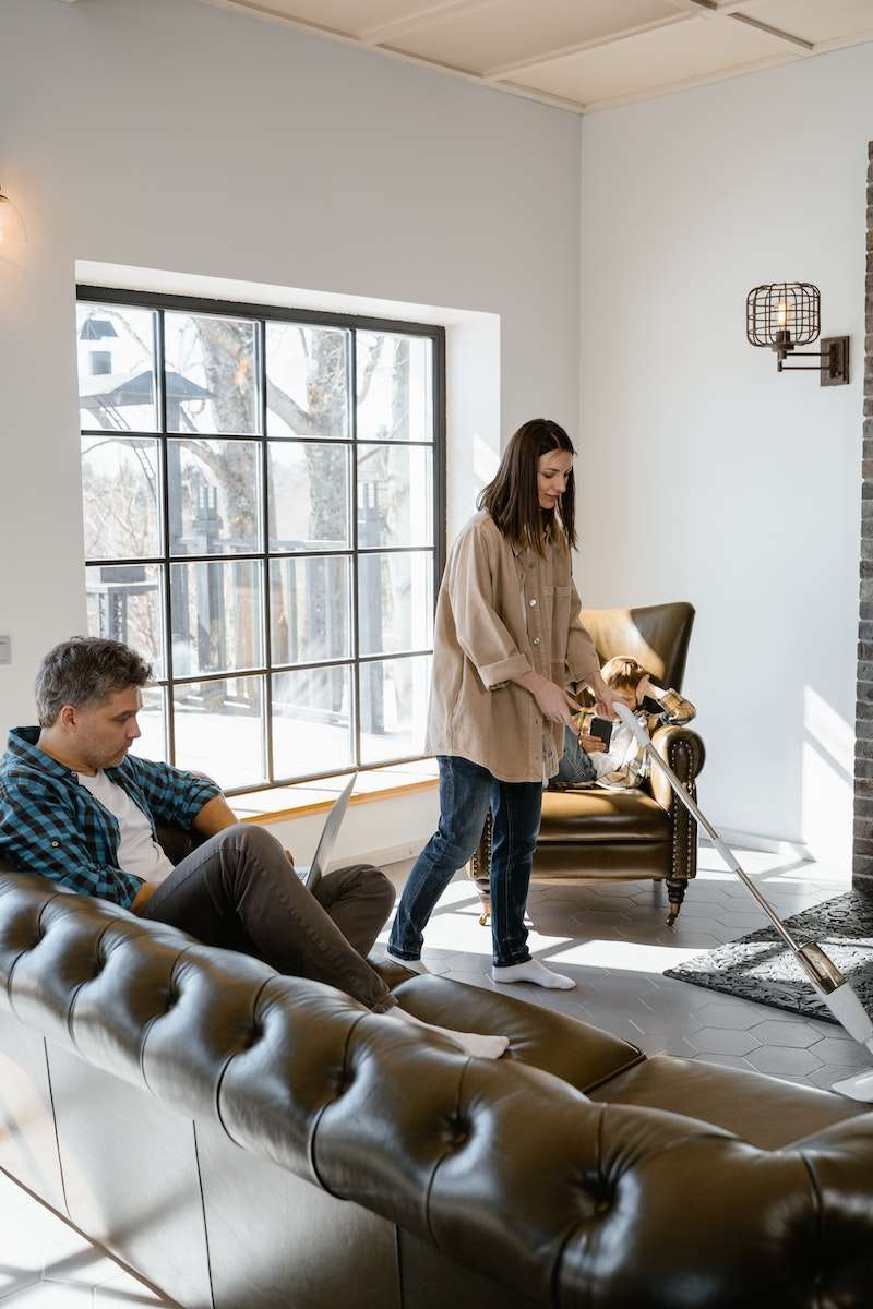 A Man Sitting on the Couch while Looking at the Woman Cleaning the Floor